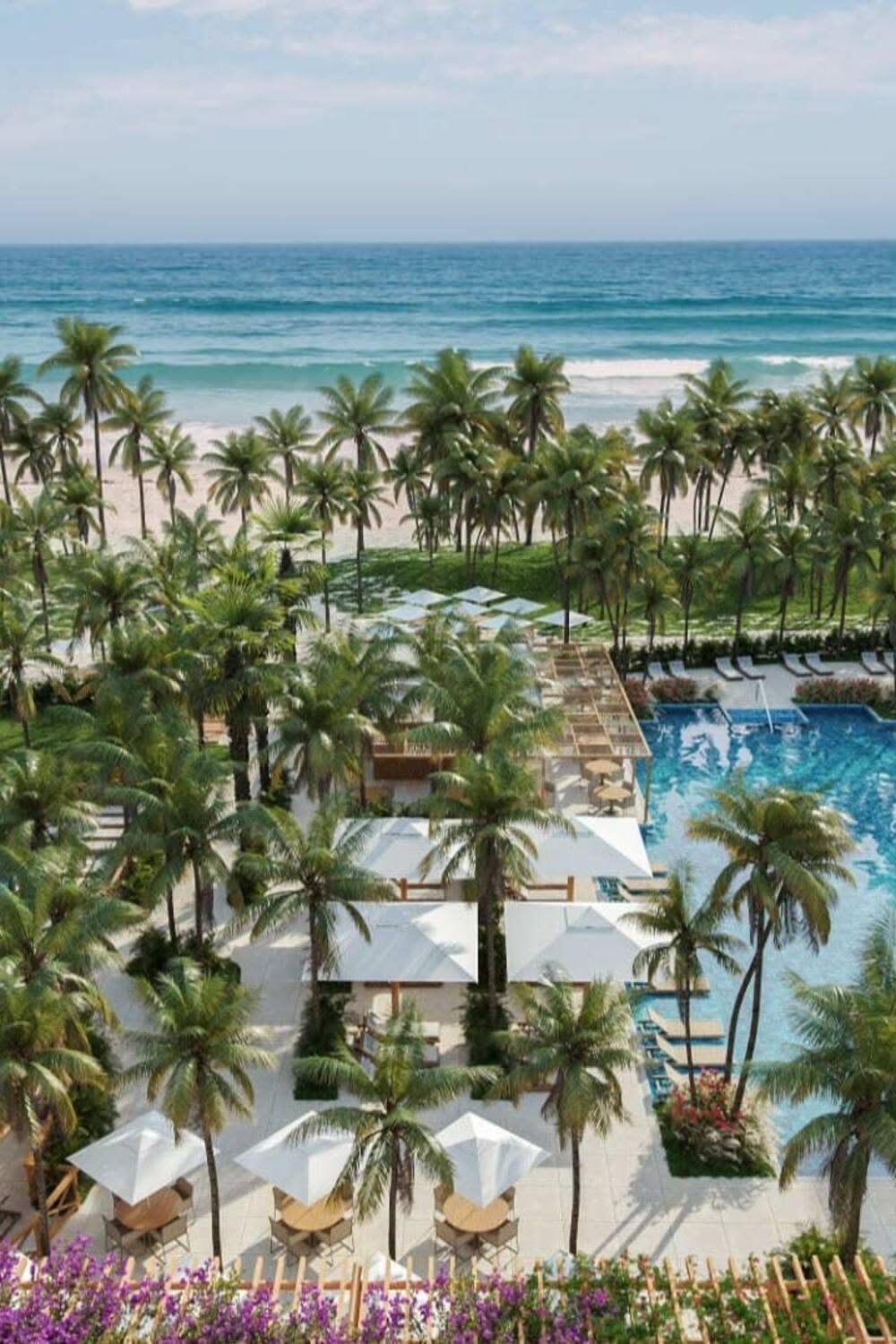 Aerial view of a tropical beach resort with a swimming pool, palm trees, and ocean.
