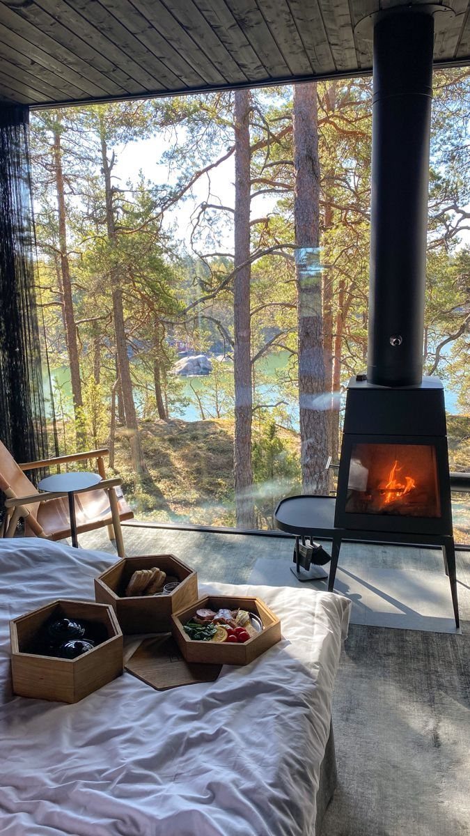 A cozy room with a wood-burning stove and snacks on a bed overlooking a forest.