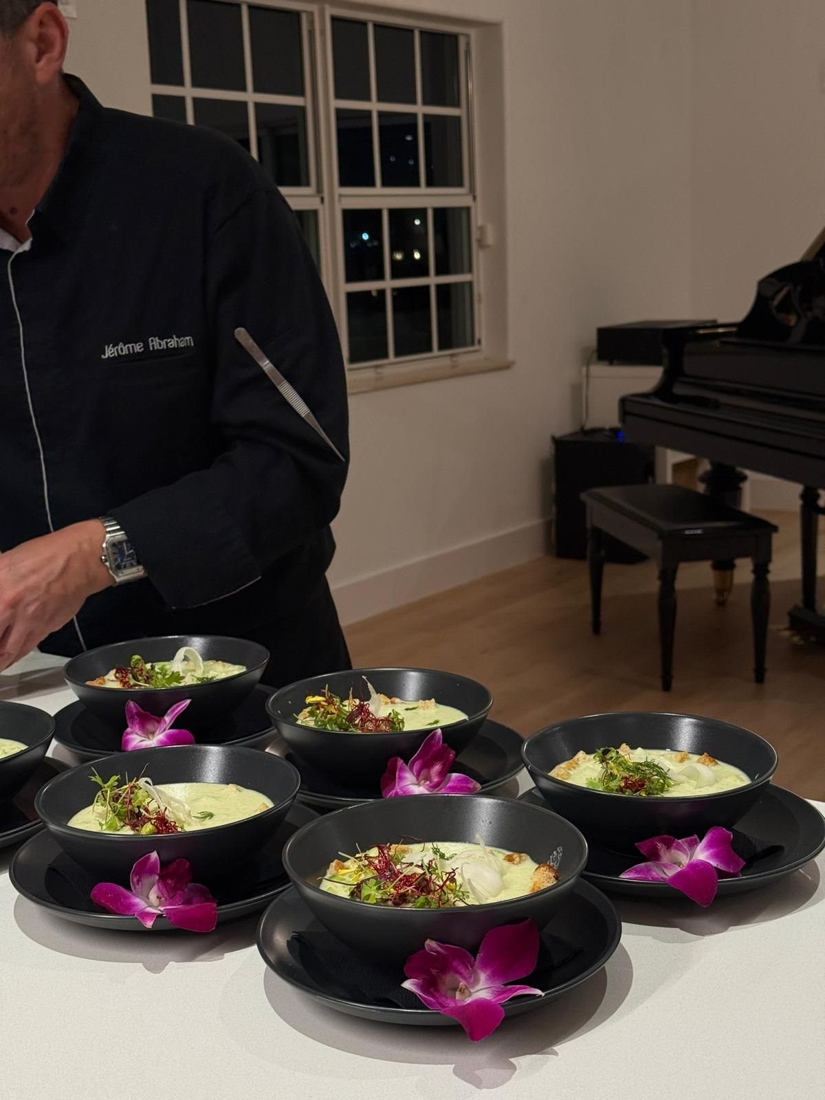 A chef preparing several bowls of garnished creamy soup on a white table.