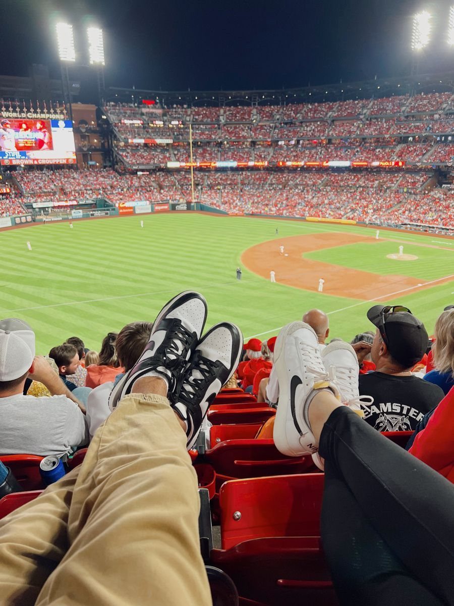 Two people's legs and feet extended towards a baseball field in a crowded stadium.