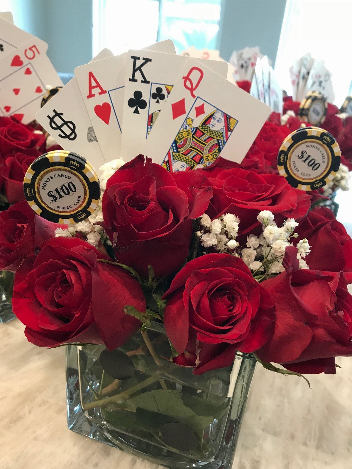 Red roses in a glass vase decorated with playing cards and poker chips.