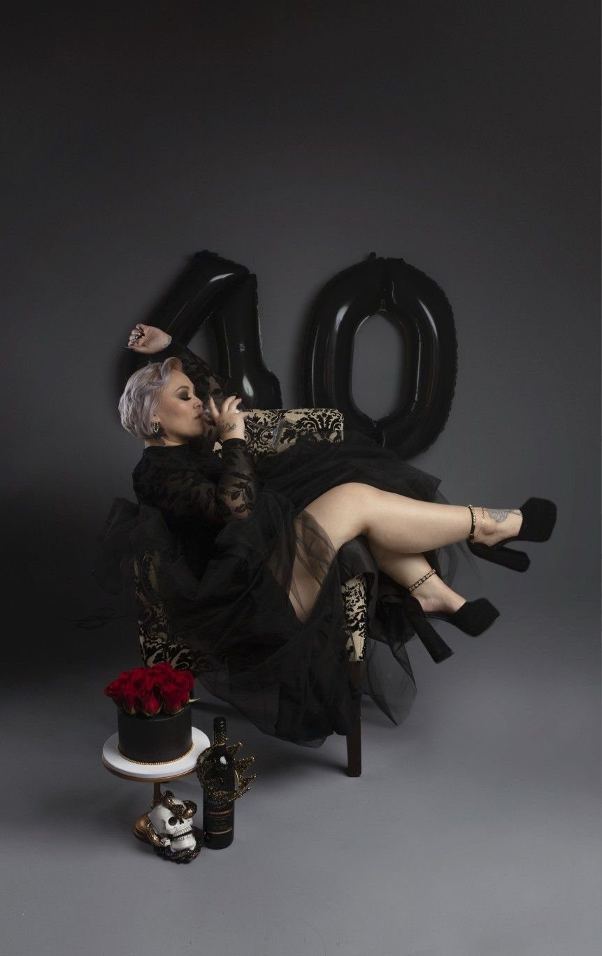 A woman in a glamorous black dress poses with '40' balloons.