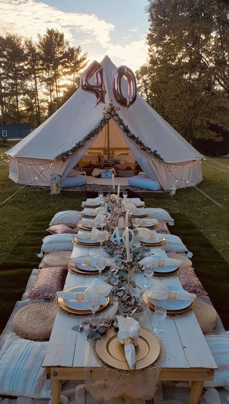 Outdoor dining table set for a celebration with a large white tent and forty balloons.