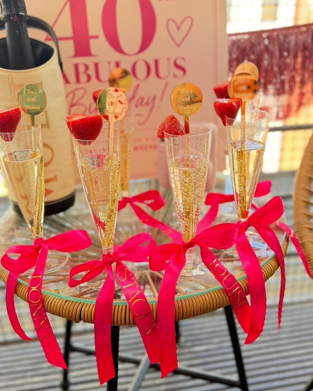 Champagne flutes with pink ribbons and strawberries on a table.