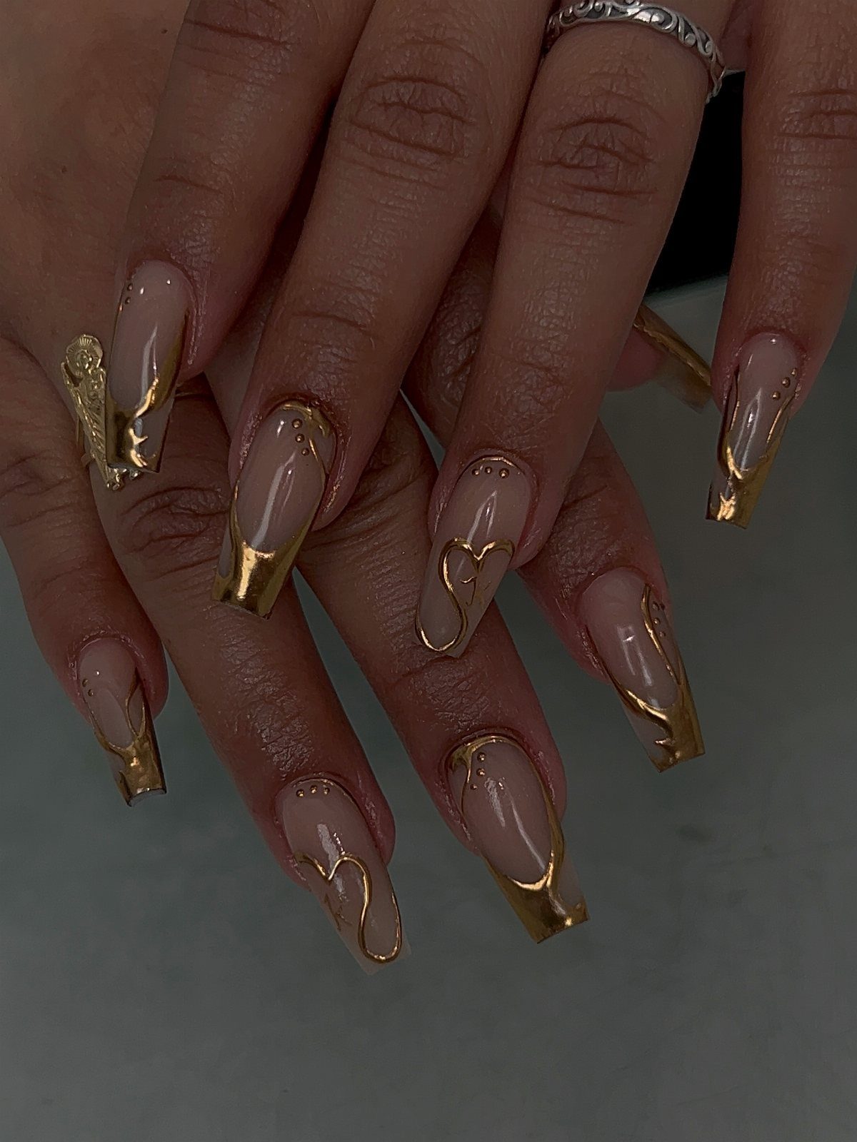 Long nude coffin nails with swirling gold metallic designs and gold foil tips.