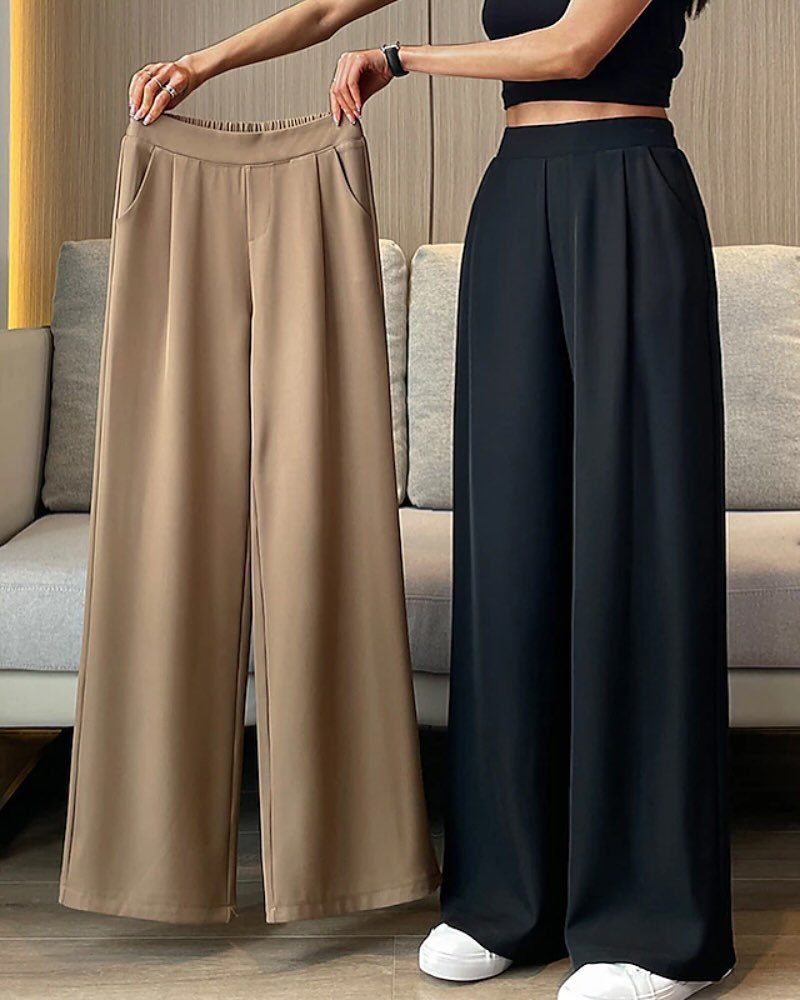A person displaying tan and black wide-leg trousers against a neutral indoor background.