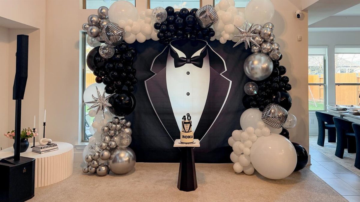 Black and white balloon arch surrounding a tuxedo graphic backdrop with a 40th birthday cake.