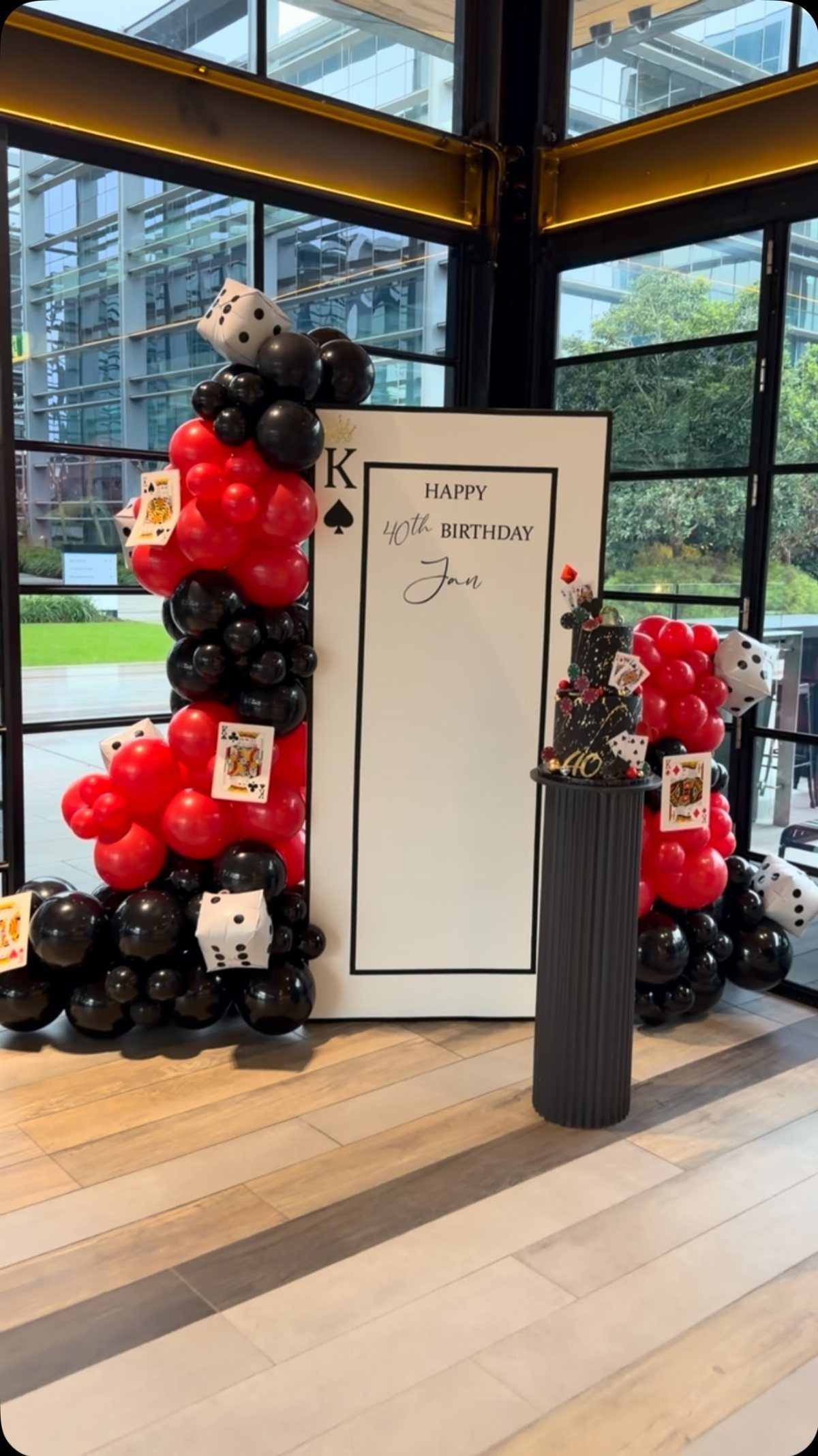 Red and black balloon arches with dice and playing cards surrounding a large birthday backdrop.