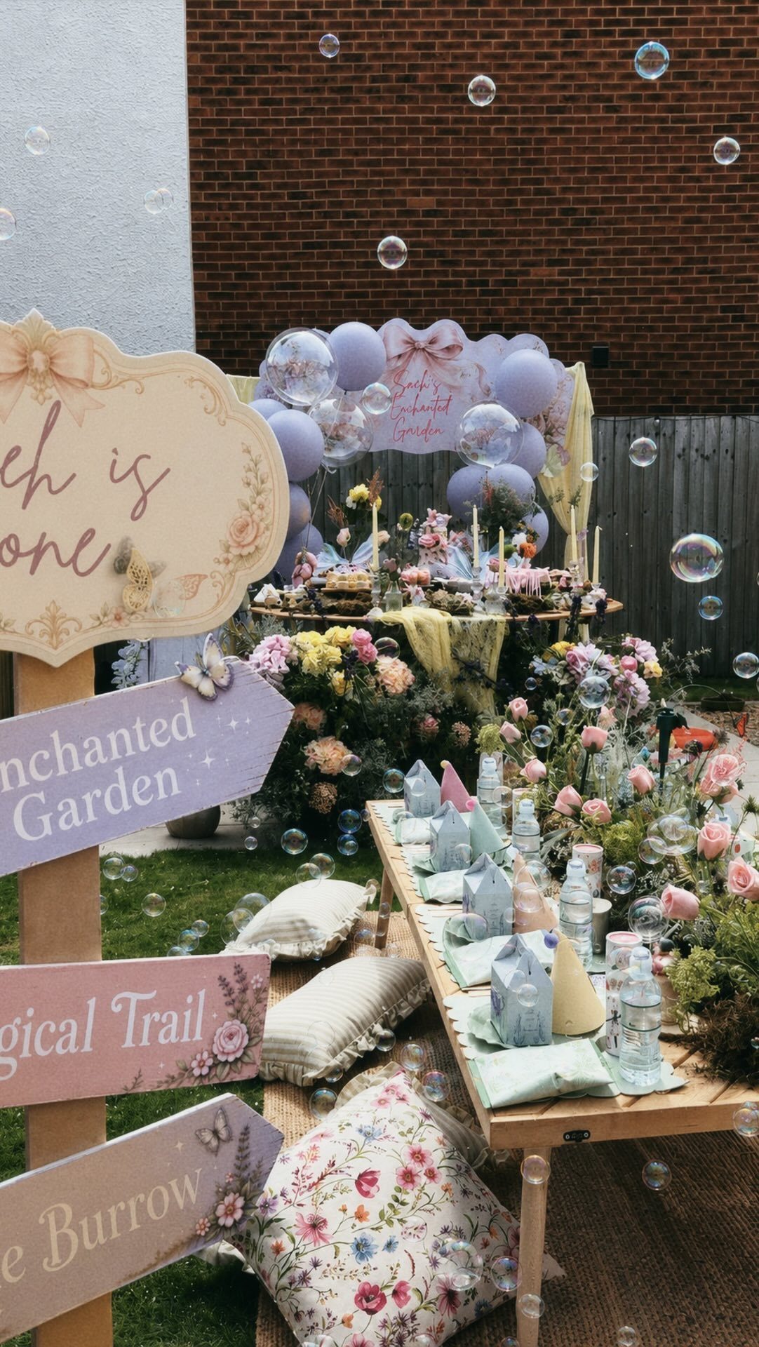 An enchanted garden party setup with low tables, floral decor, and whimsical wooden signs.