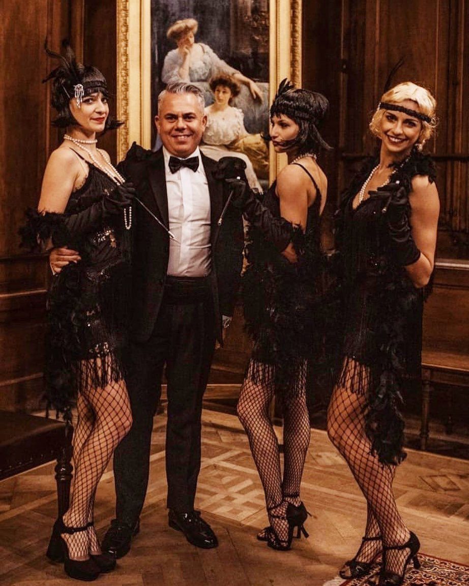Four people dressed in Roaring Twenties flapper and tuxedo attire posing indoors.