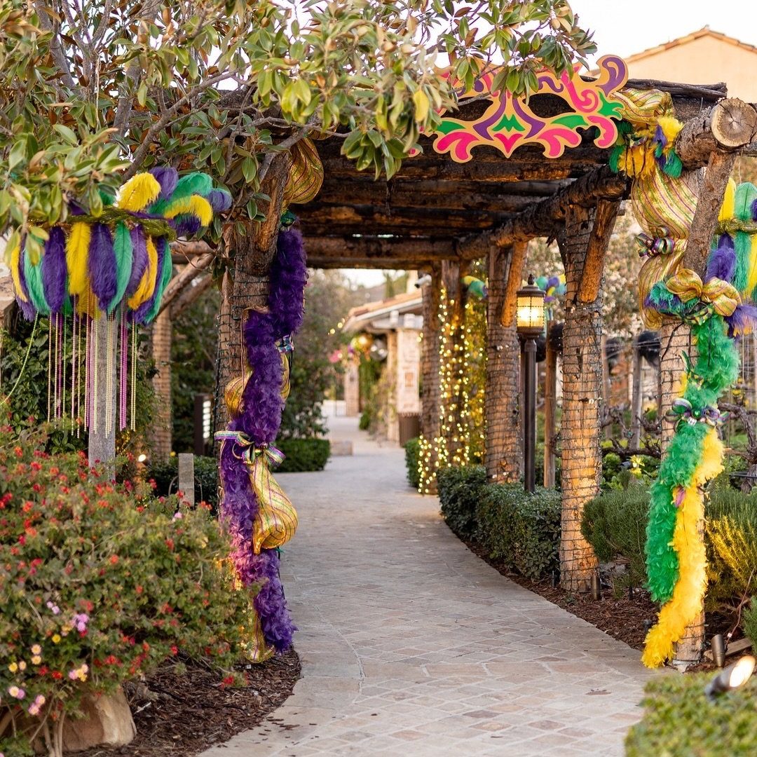 A stone walkway under a pergola decorated with purple, green, and gold Mardi Gras decorations.