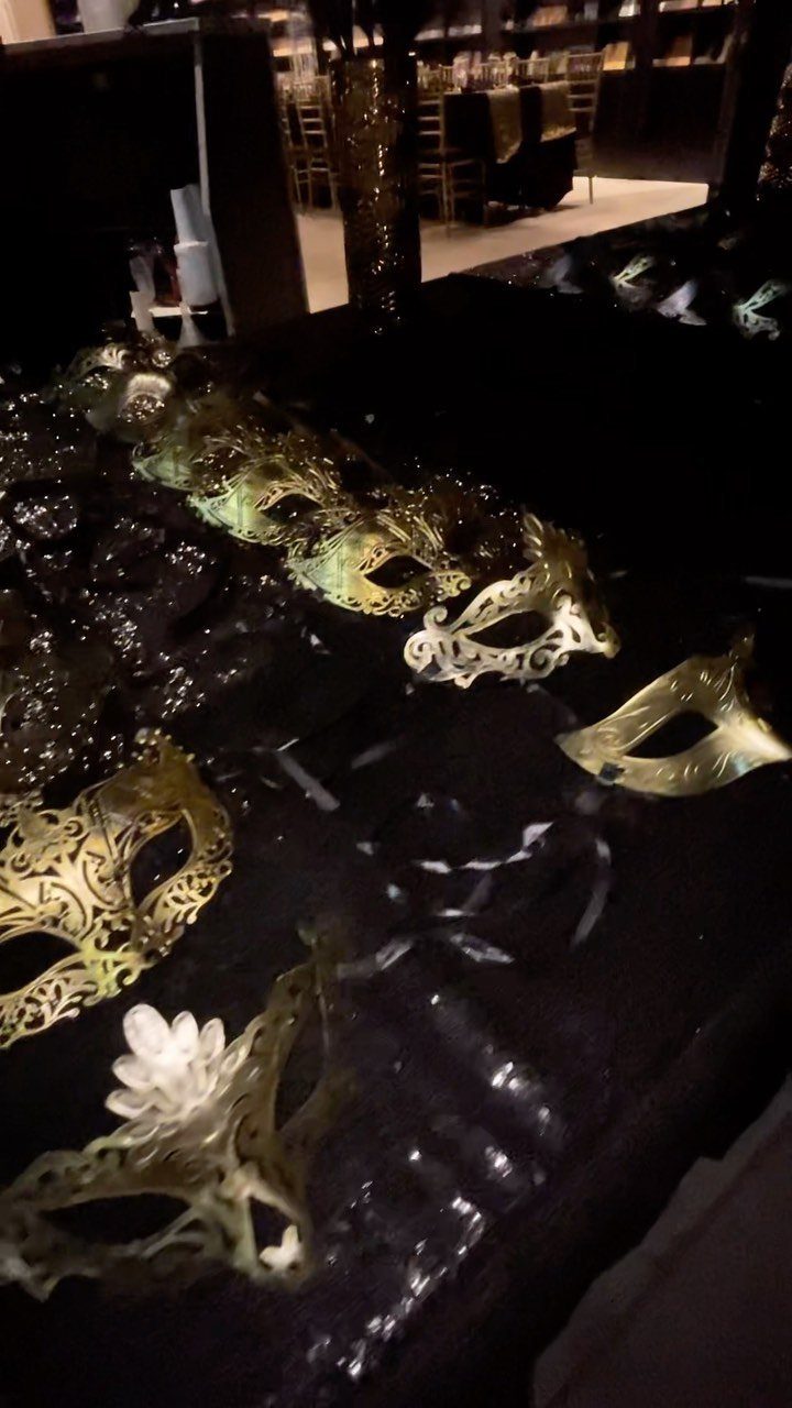 Ornate gold and silver masquerade masks resting on a dark, reflective table surface.