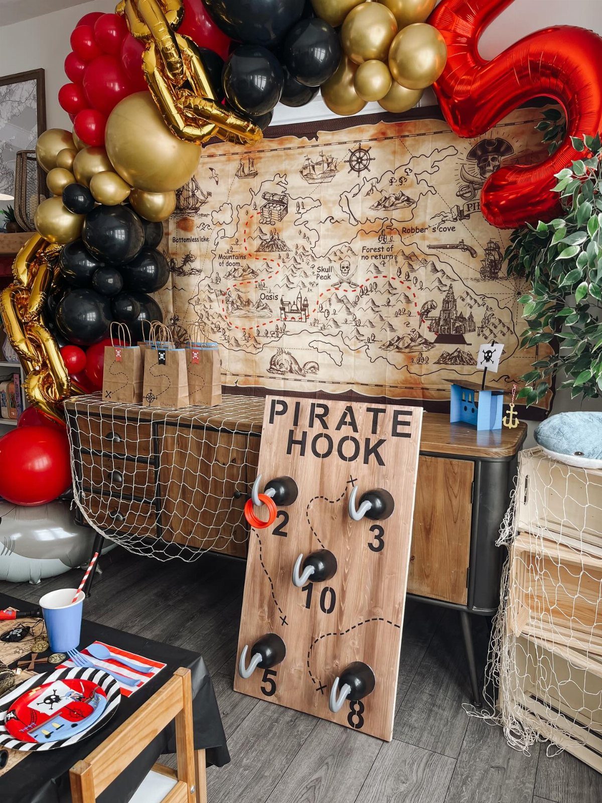 Pirate themed party decorations including a treasure map backdrop, balloon arch, and hook game.