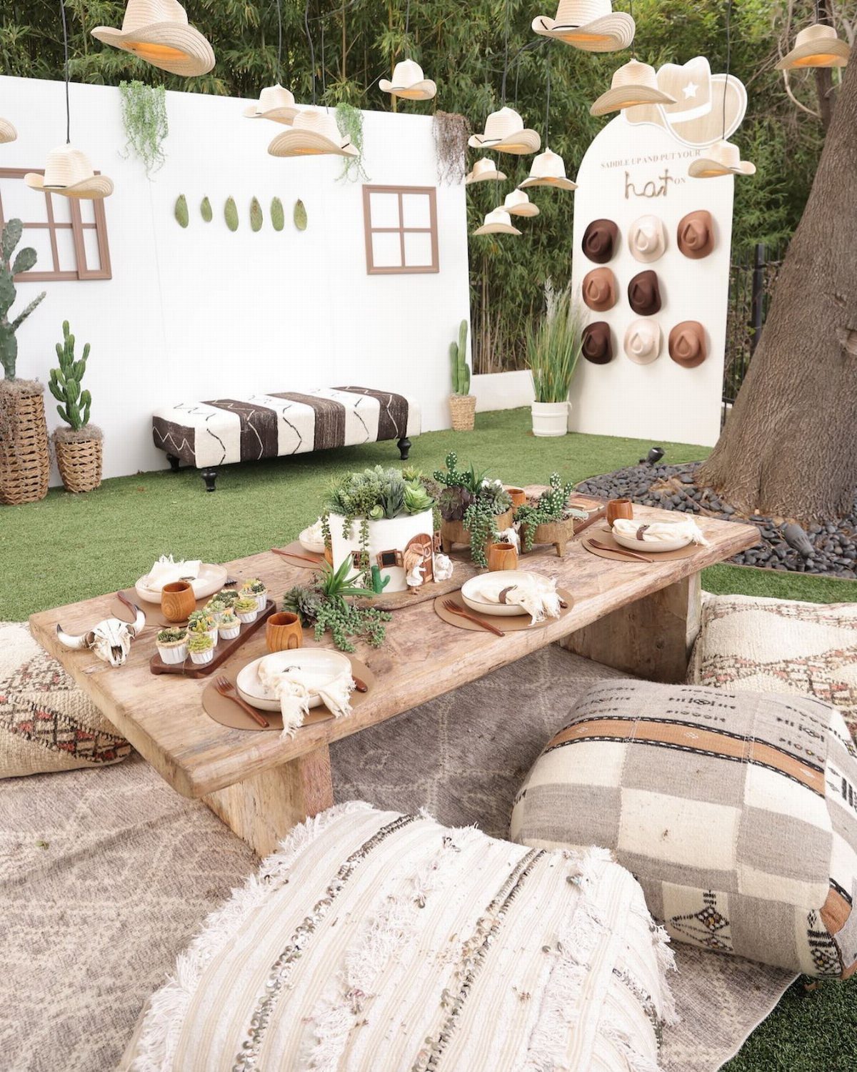 A rustic outdoor low table setting with cushions, succulents, and cowboy hat decorations.