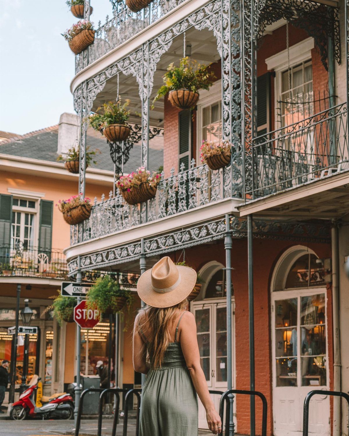Woman in a sun hat looking at historic buildings with ornate wrought-iron balconies in New Orleans.