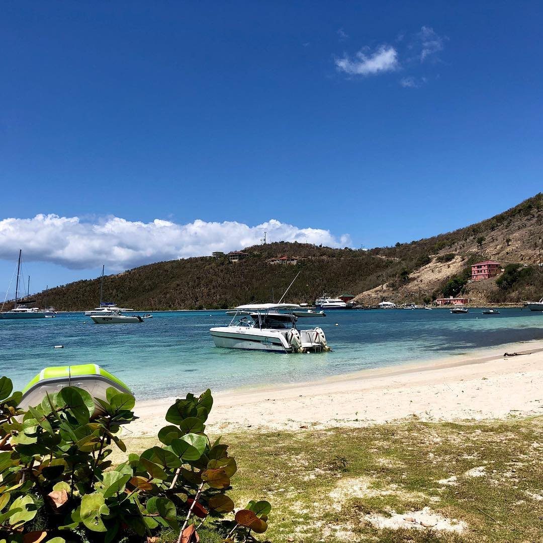 Turquoise ocean water and white sand beach with boats anchored near green hills.