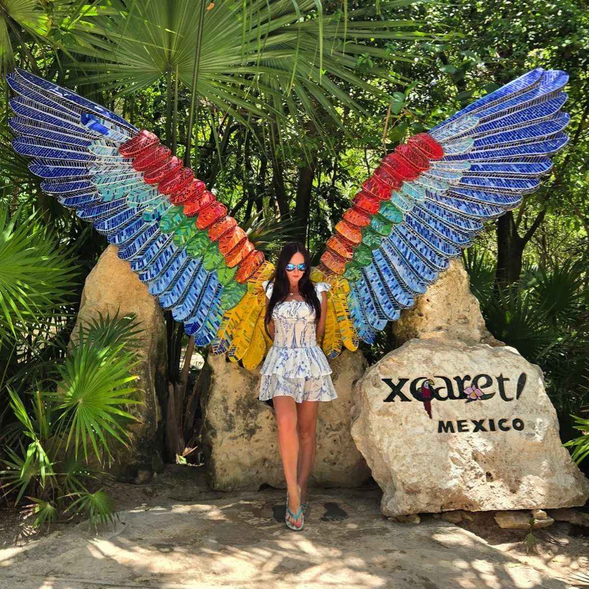 Woman posing in front of large colorful mosaic wings at Xcaret Mexico.