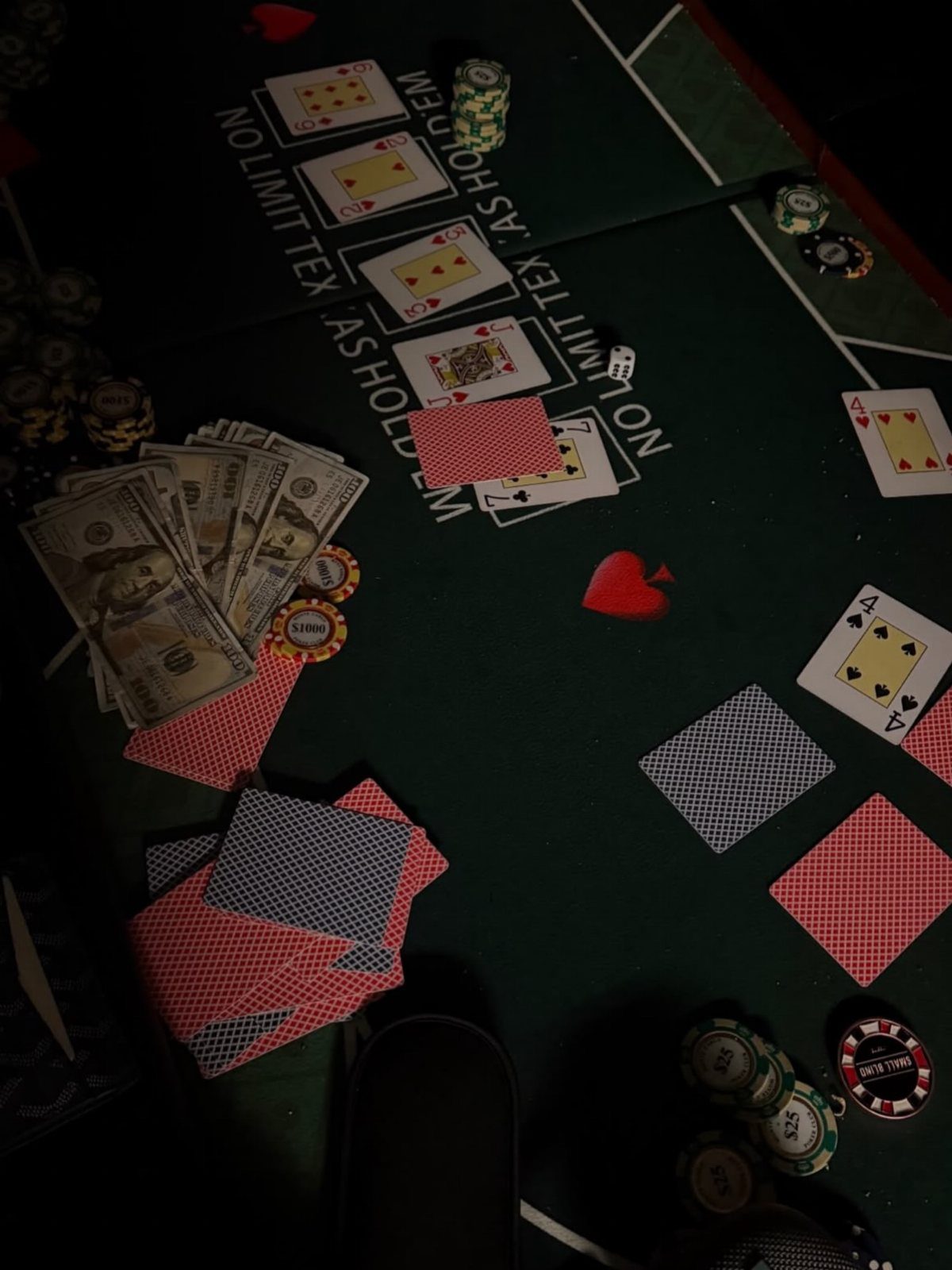 Playing cards, poker chips, and stacks of dollar bills scattered on a green felt poker table.