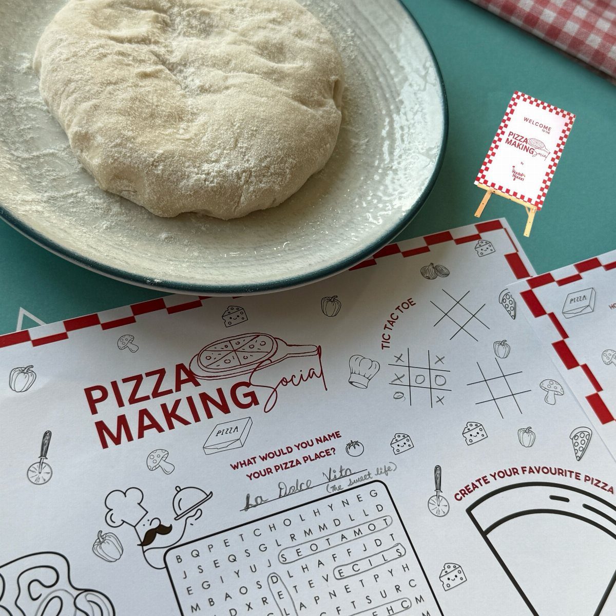 Pizza dough on a plate next to a themed pizza making activity placemat.