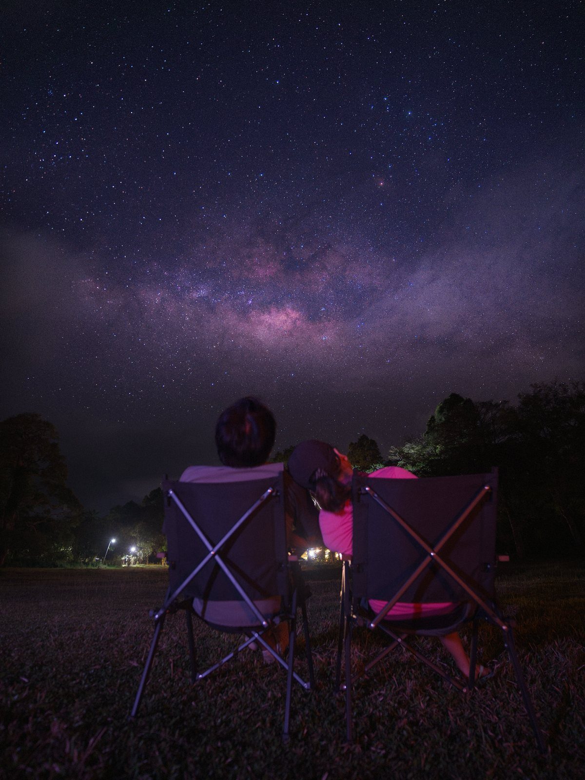 Two people sitting in chairs under a vast, starry Milky Way night sky.