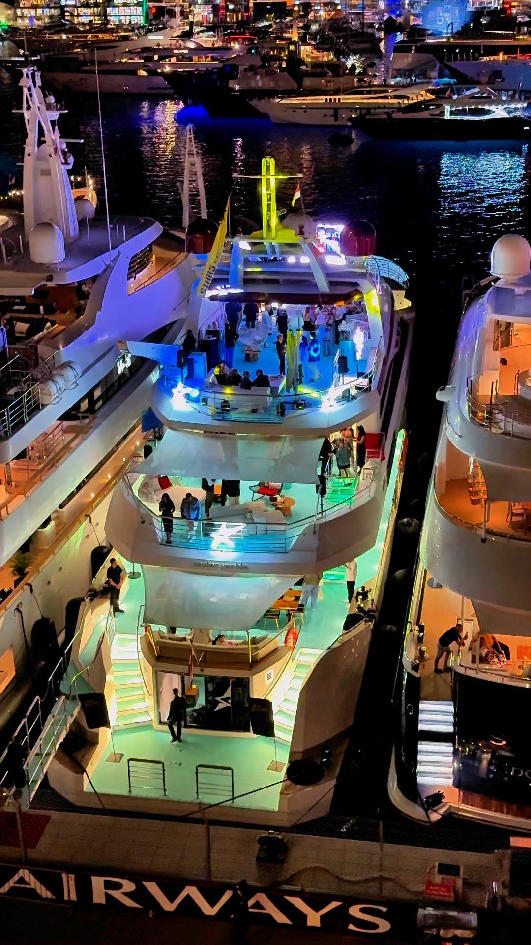Large luxury yacht illuminated with blue lights docked in a marina at night.