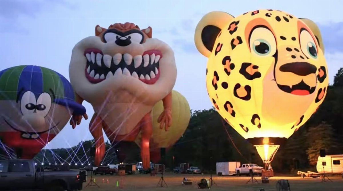 Large character-shaped hot air balloons inflated on a field during twilight.