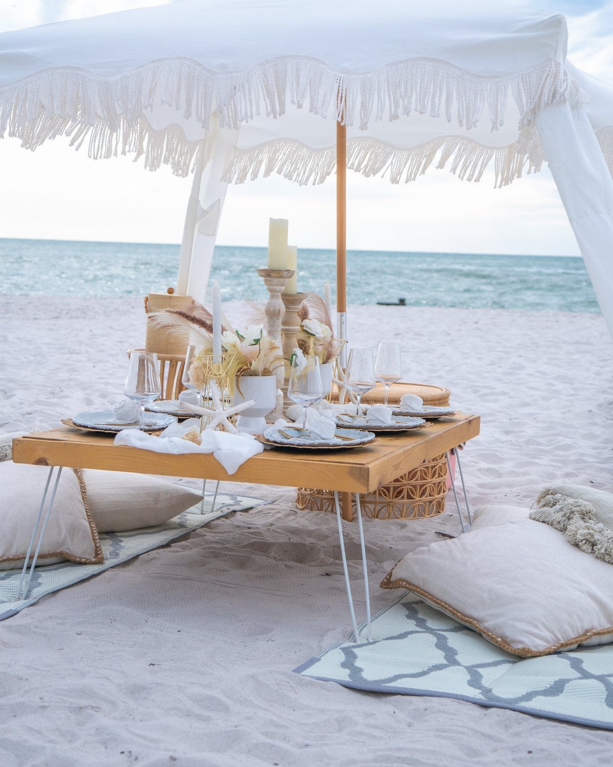 A luxury low wooden table set for a picnic on a white sand beach.