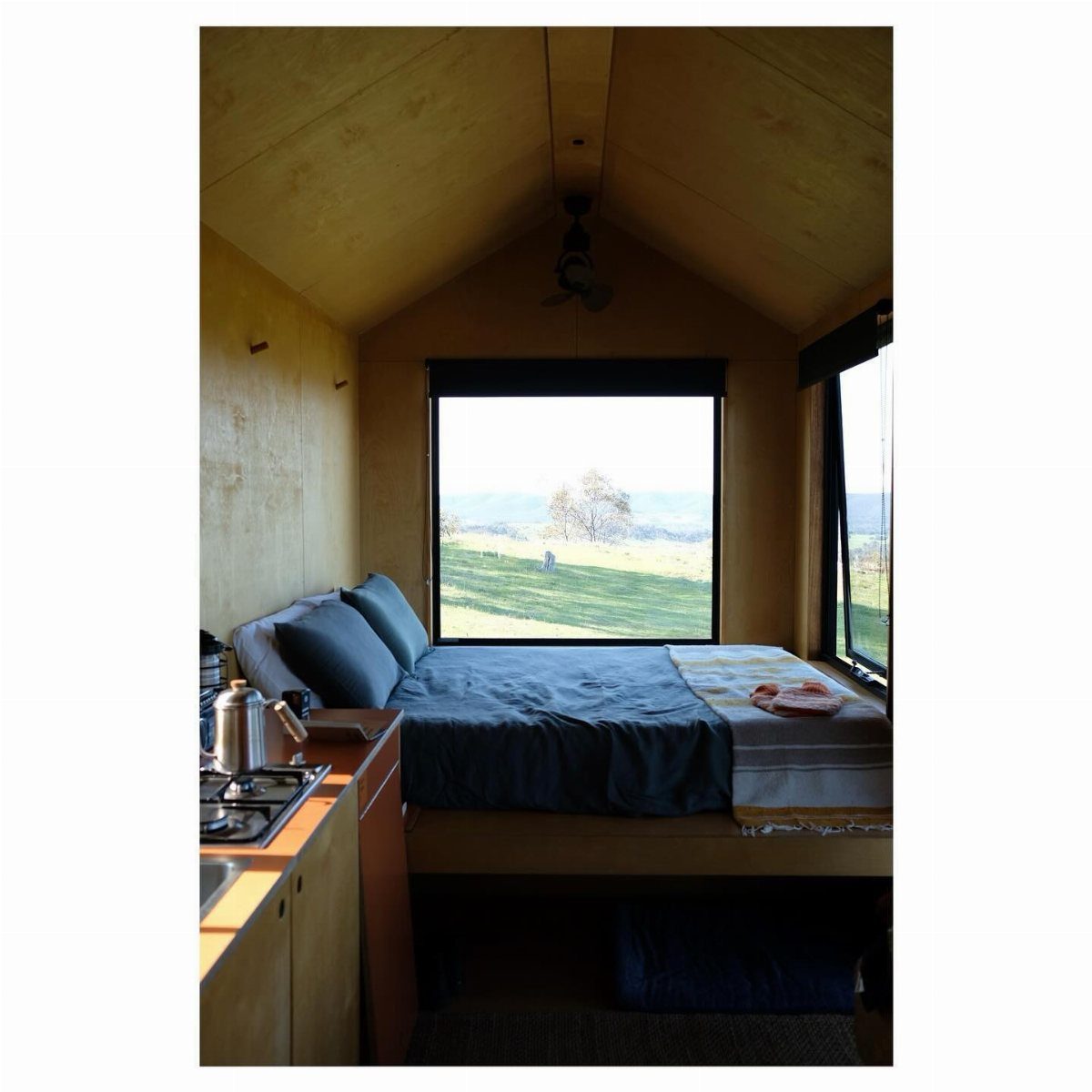 A cozy wooden cabin interior with a bed and window overlooking a green landscape.