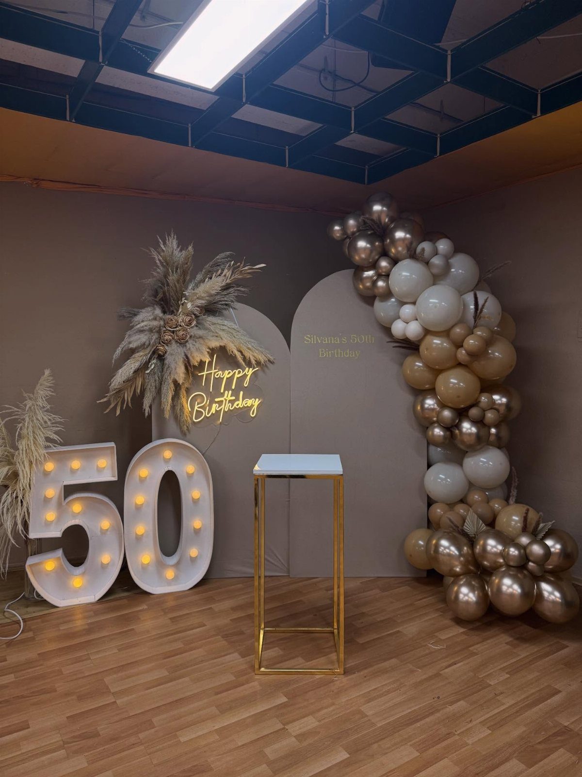 Large marquee numbers fifty and gold balloon arch decorating a birthday party venue.