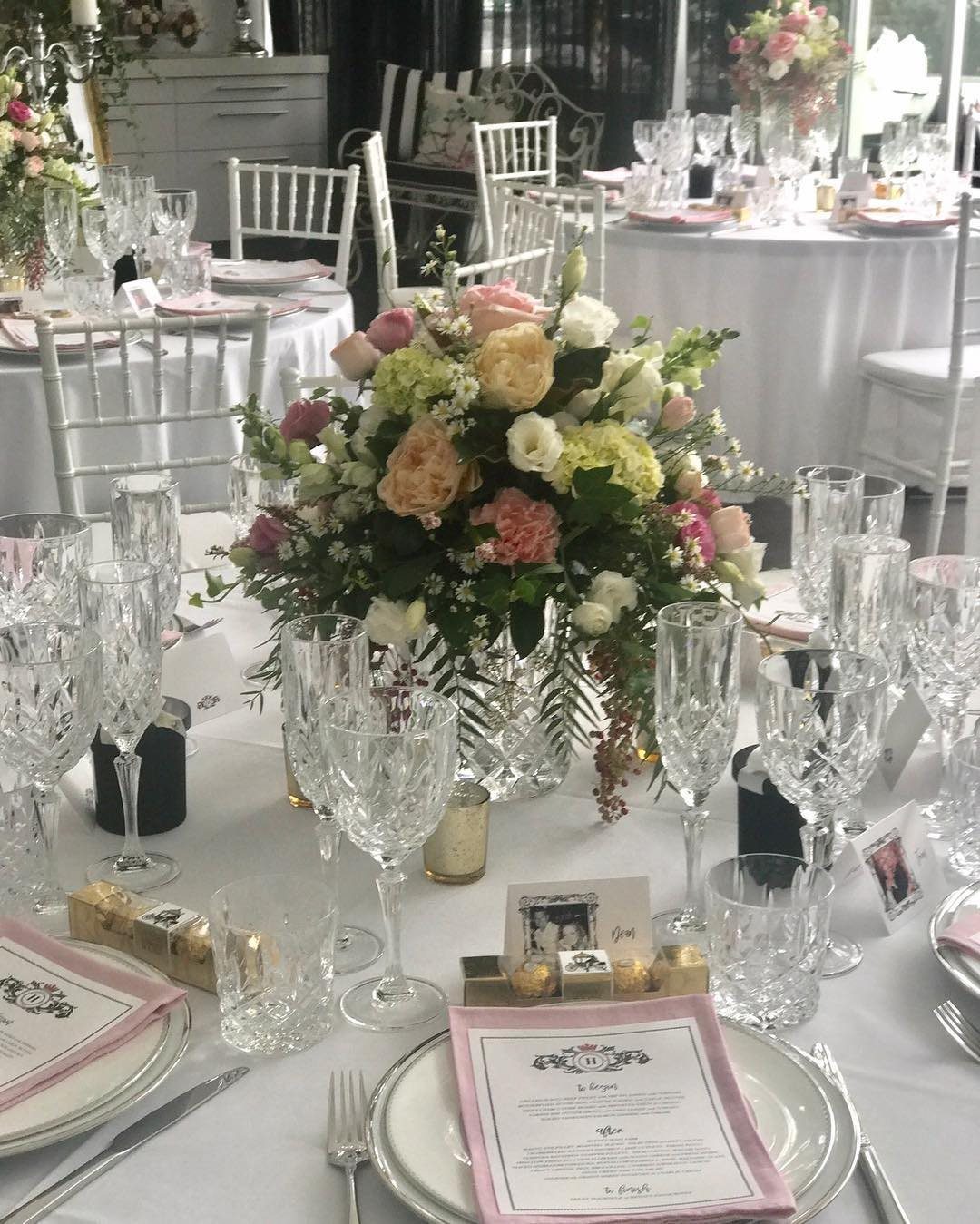 Formal table setting with floral centerpiece, crystal glasses, and pink napkins on white plates.