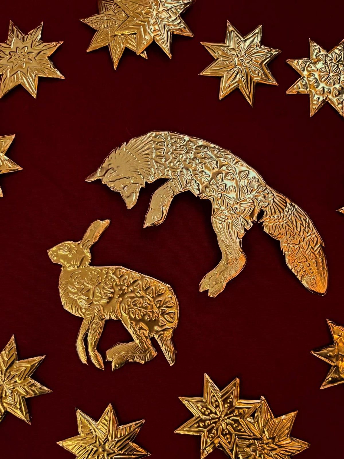 Gold foil animal and star cutouts arranged on a dark red surface.