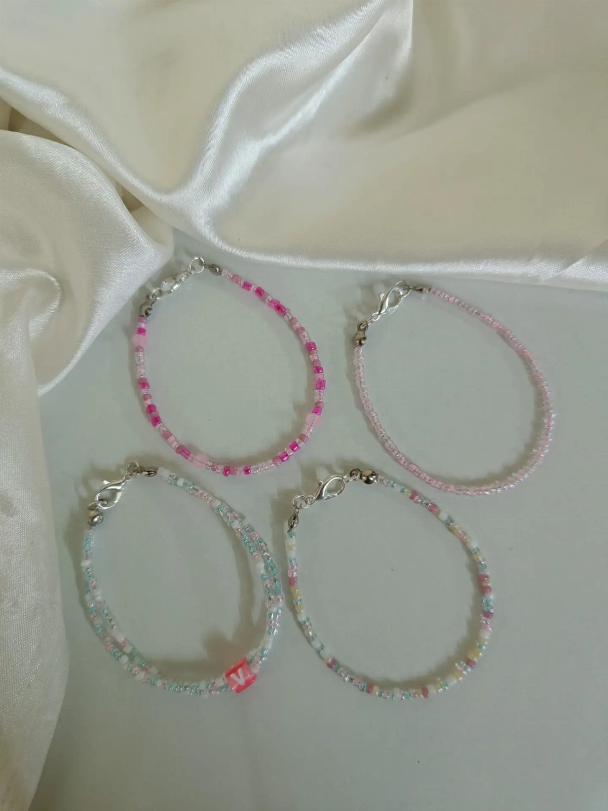 Four colorful beaded bracelets resting on a white surface with draped satin fabric.