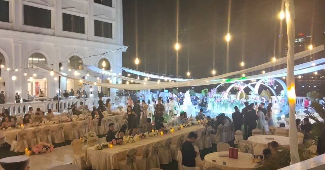 An outdoor rooftop event space with long banquet tables, white linens, and warm string lights.