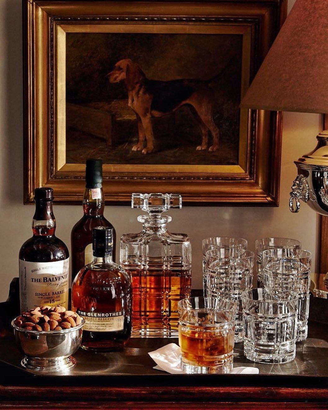 Whiskey bottles, a crystal decanter, and glasses arranged on a tray with almonds.