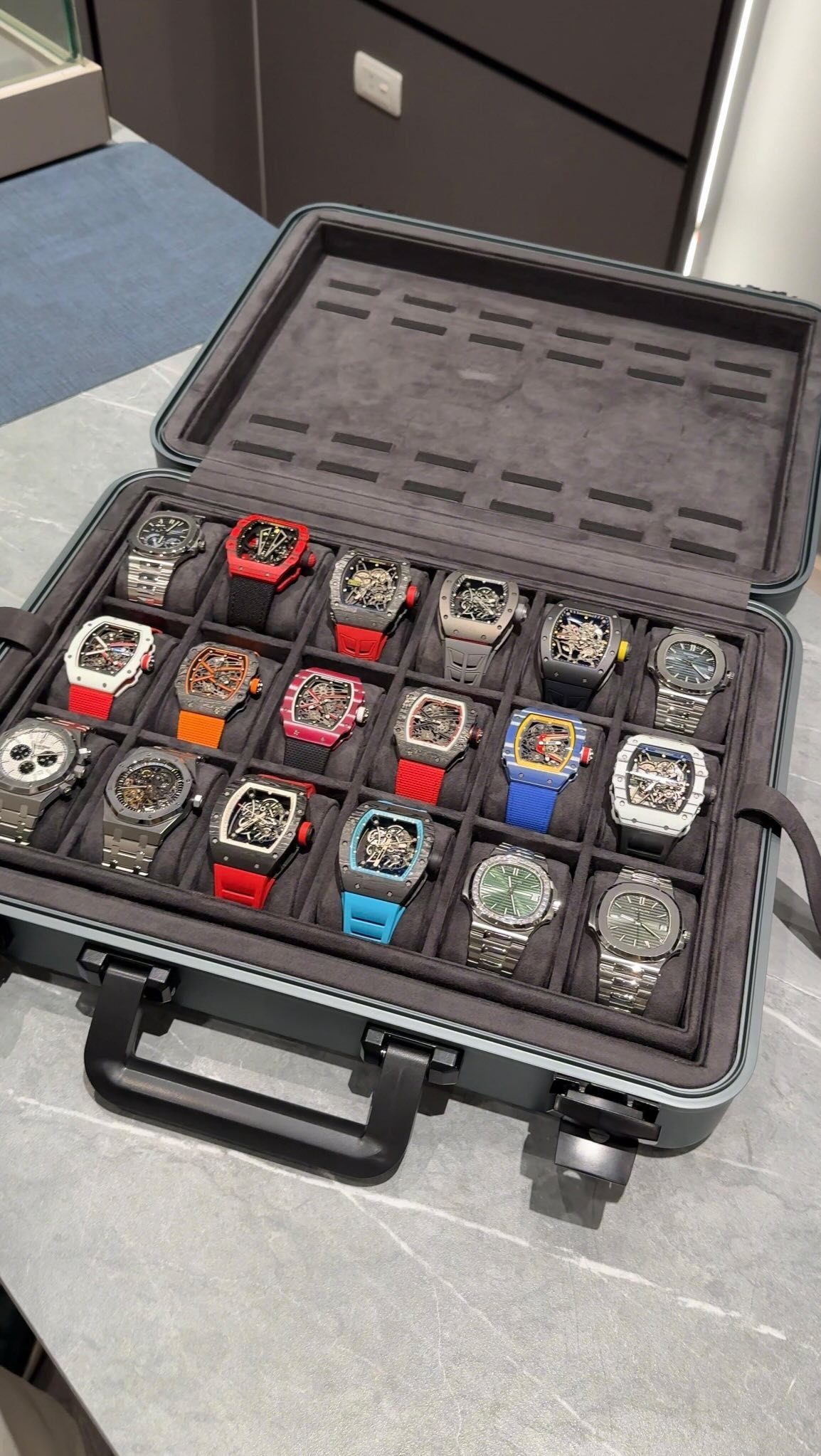 A collection of various colorful wristwatches organized inside a grey protective carrying case.