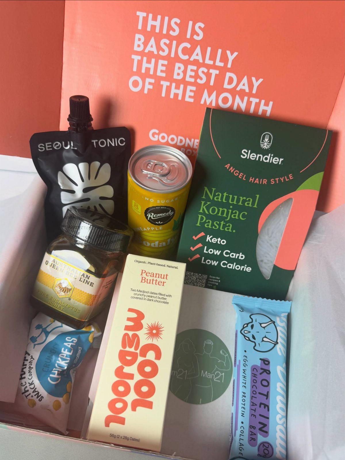 An open orange subscription box filled with various packaged snacks and food items.