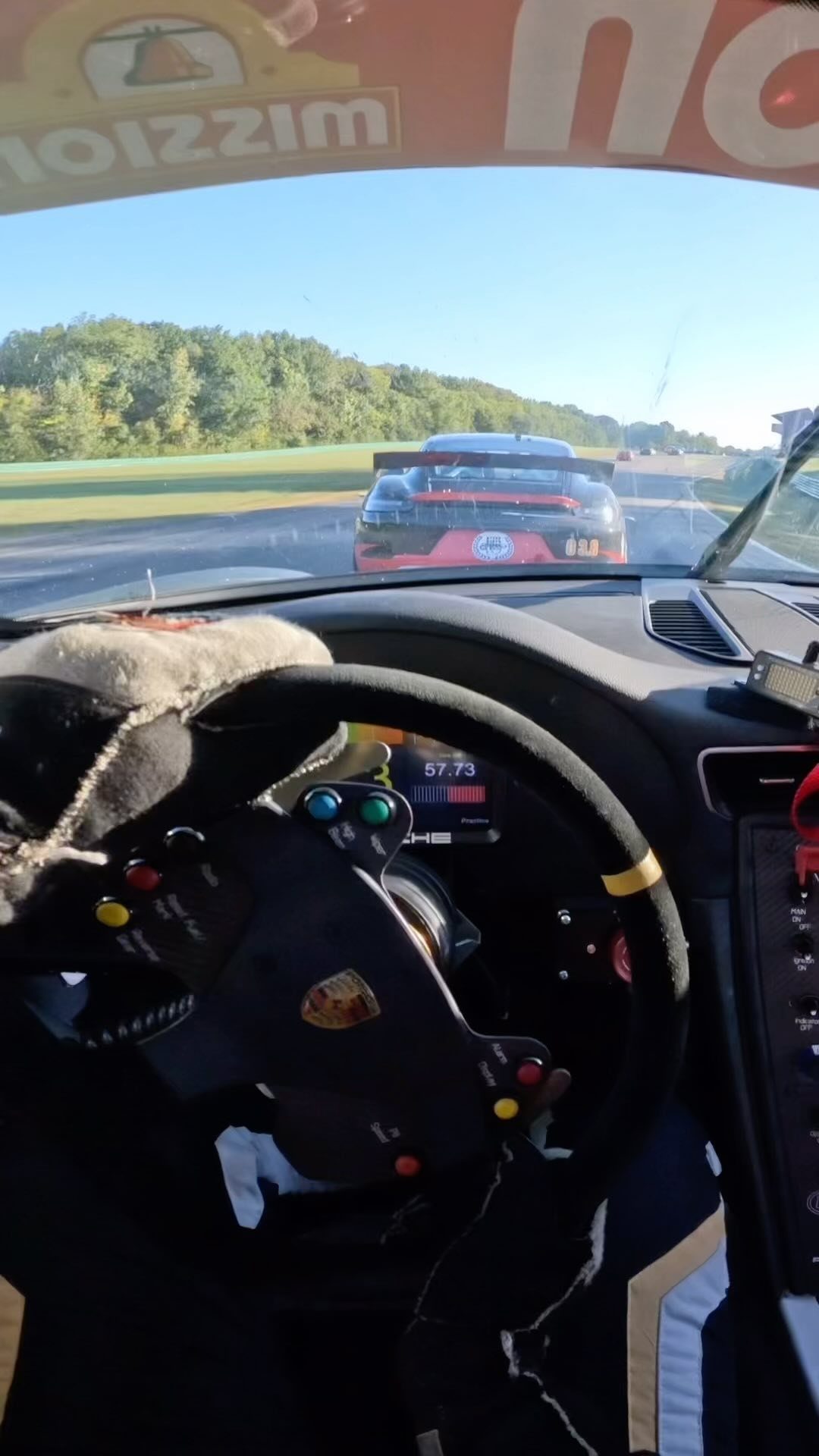 Racing steering wheel inside a car cockpit looking at another racecar on a track.