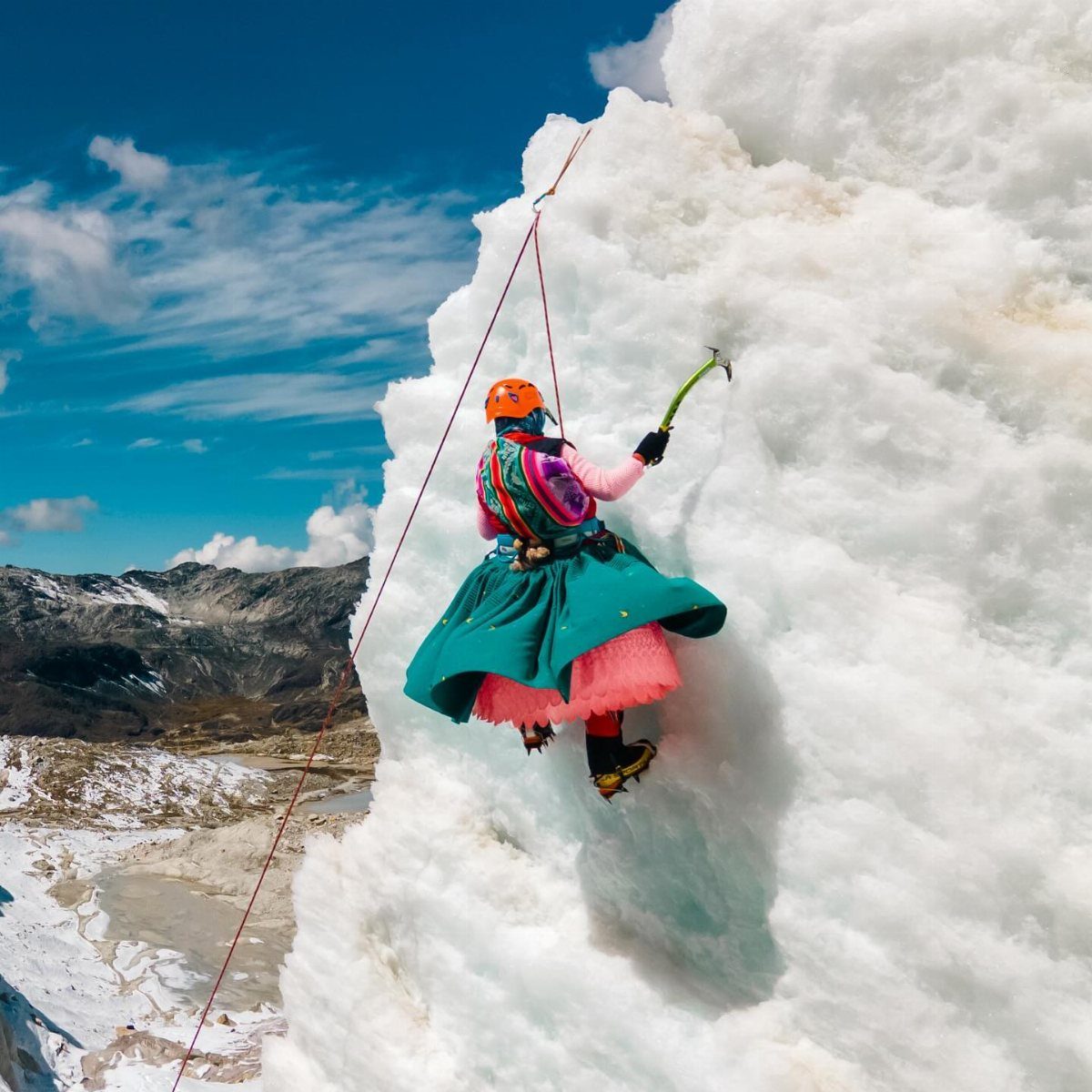 A person in a teal skirt and pink top ice climbing a massive white glacier.