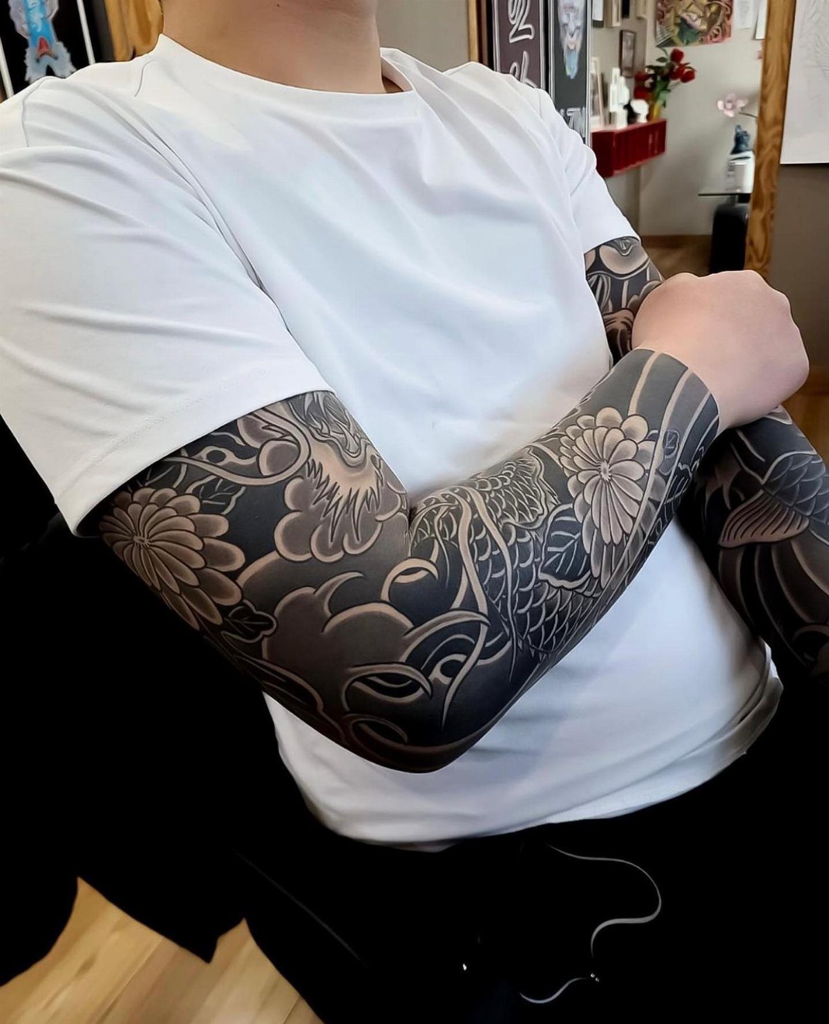 A person in a white t-shirt showcasing a detailed black and grey floral sleeve tattoo.