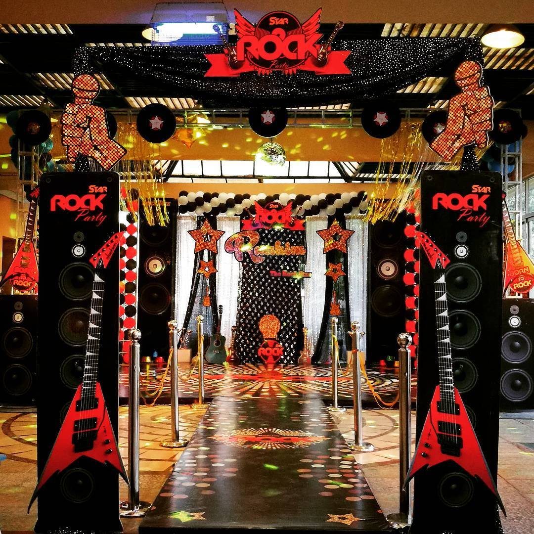 Rock themed party entrance with large speakers, red guitars, and a star-patterned runway.