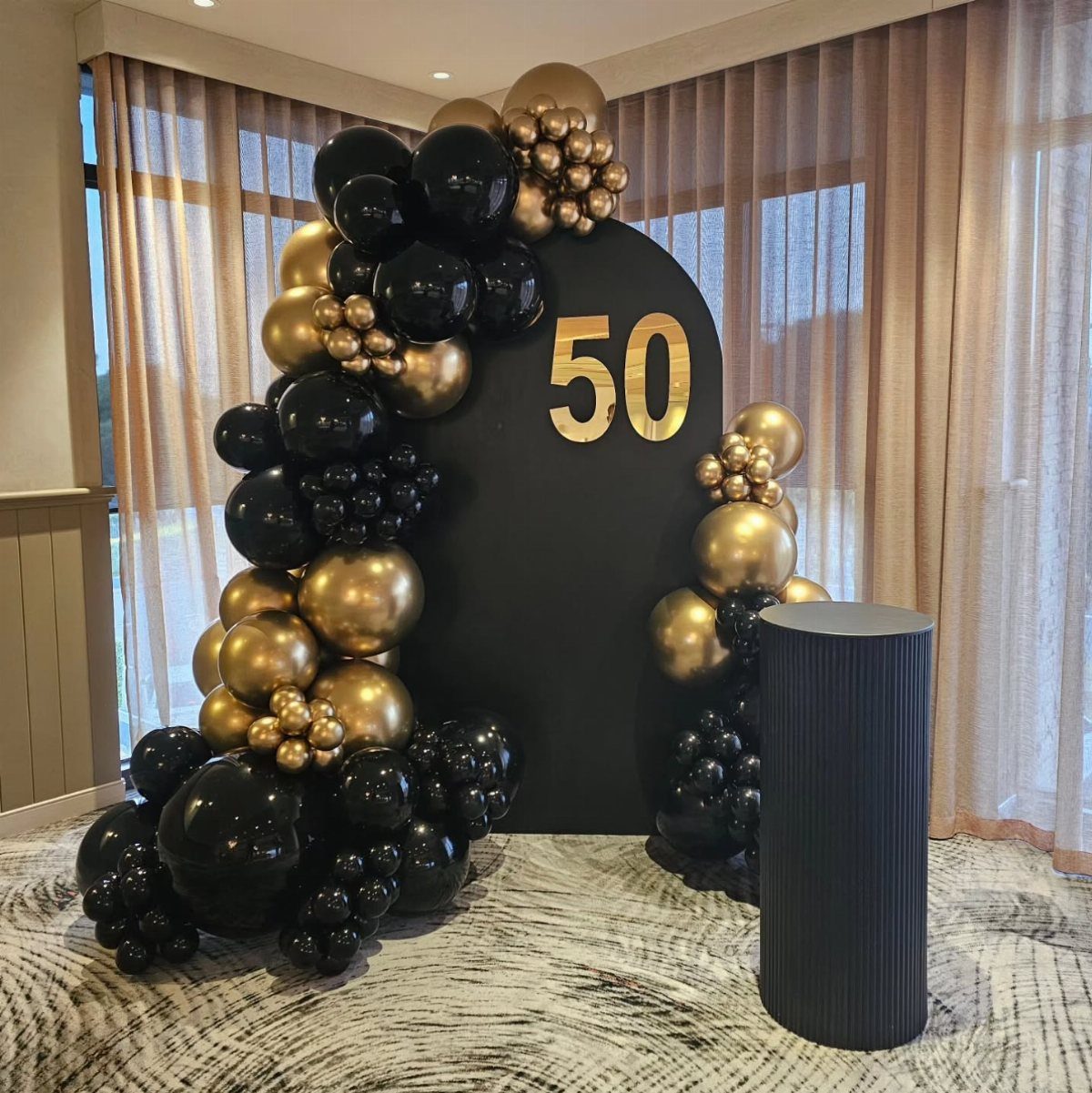 Black and gold balloons decorating a large black arch with the number 50 printed on it.