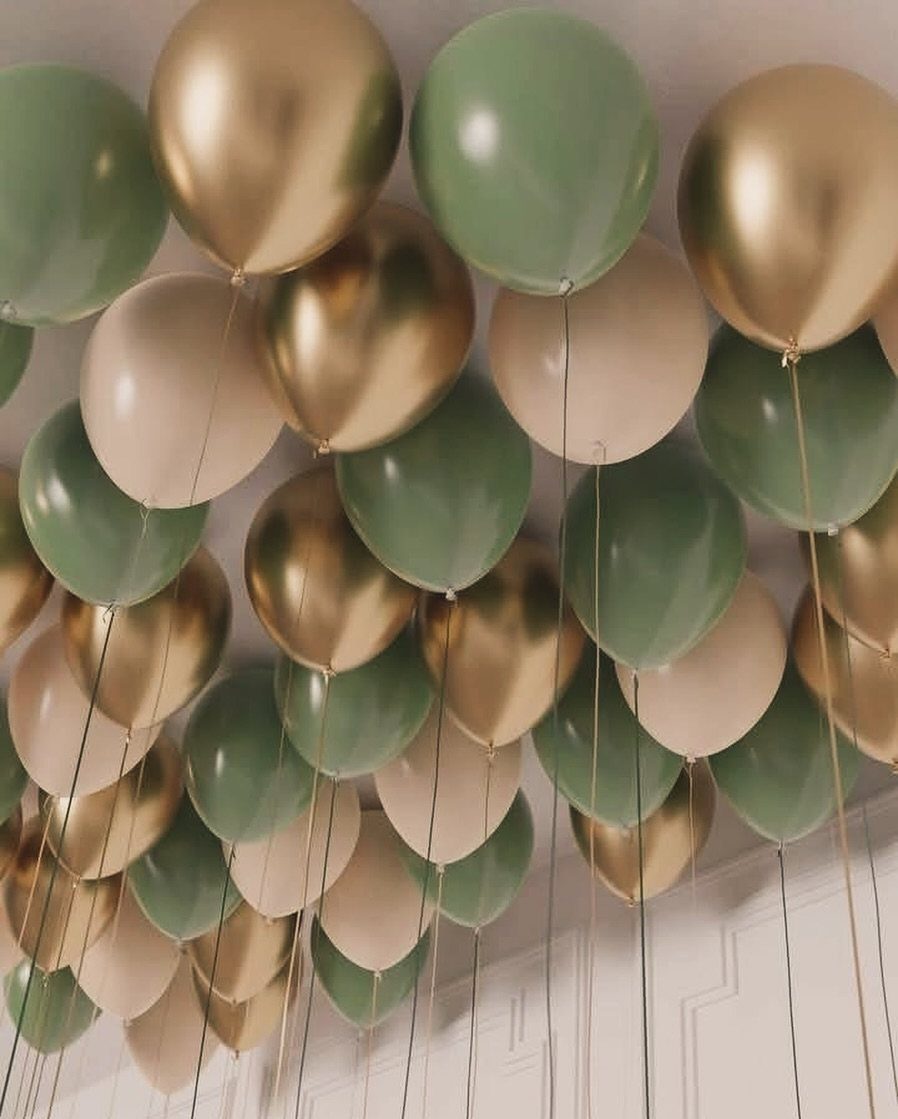 Gold, sage green, and cream balloons floating against a white ceiling with hanging ribbons.