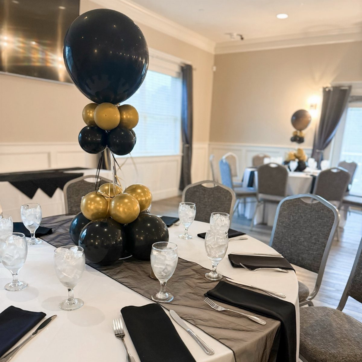 Black and gold balloon centerpiece on a decorated banquet table in a bright room.