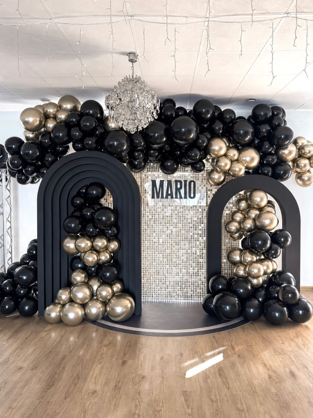 Black and gold balloon arches framing a silver sequin backdrop with the name Mario.