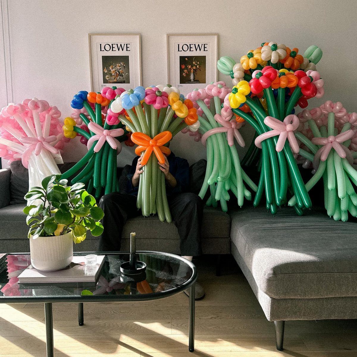 Colorful balloon flower bouquets with green stems and large bows arranged on a grey sofa.