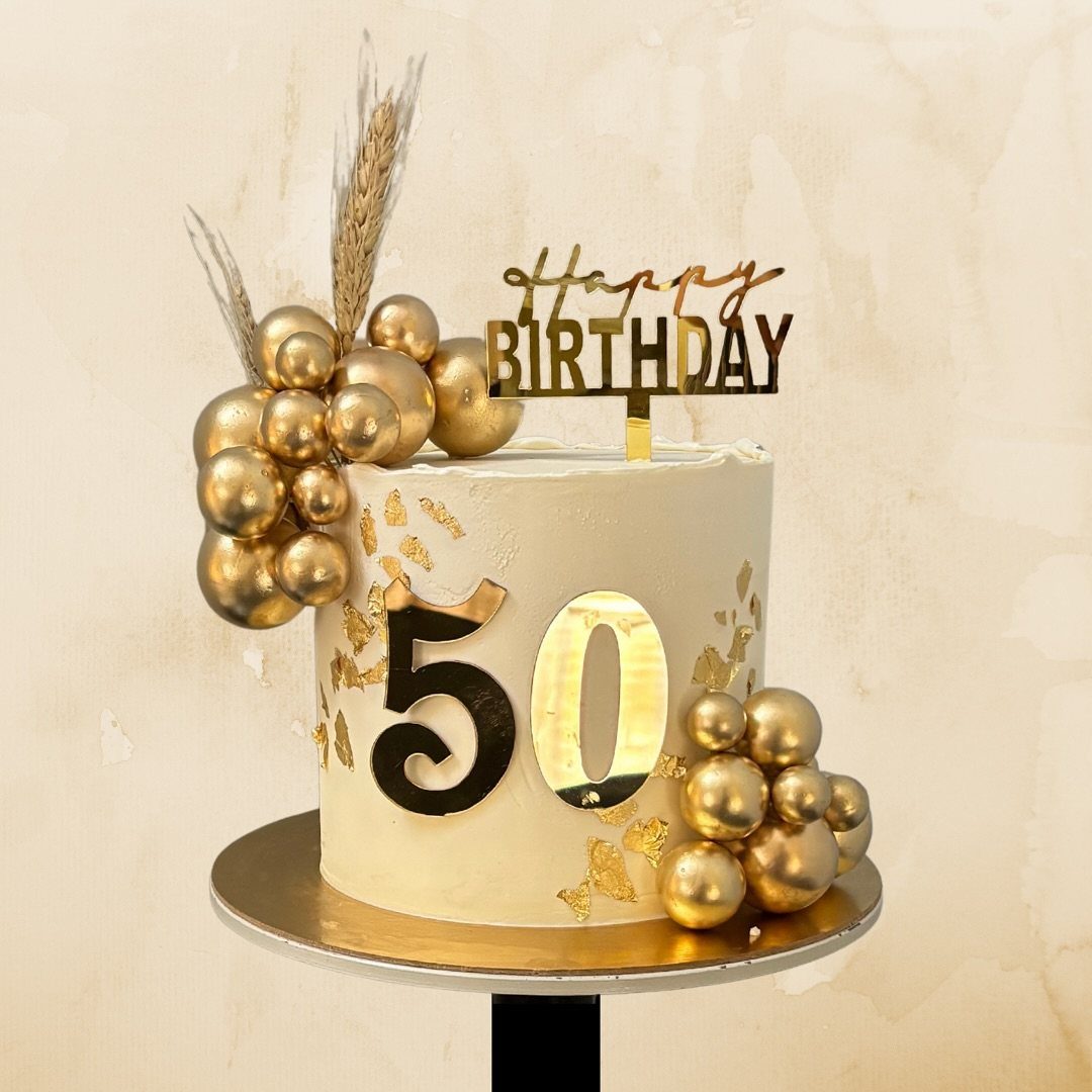 White birthday cake decorated with gold spheres, gold leaf, and a fifty number topper.