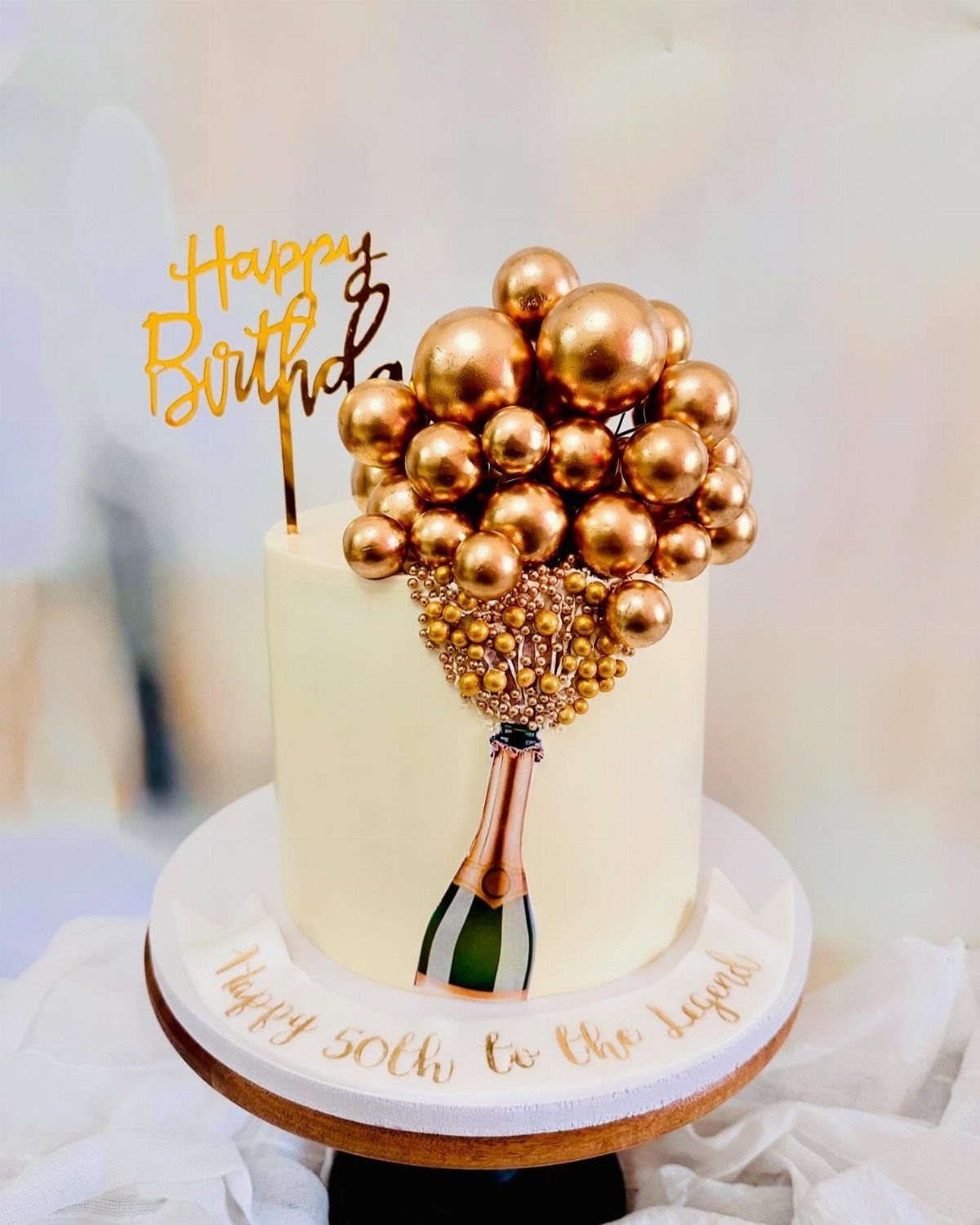 White birthday cake featuring a champagne bottle design with gold bubble spheres and a topper.