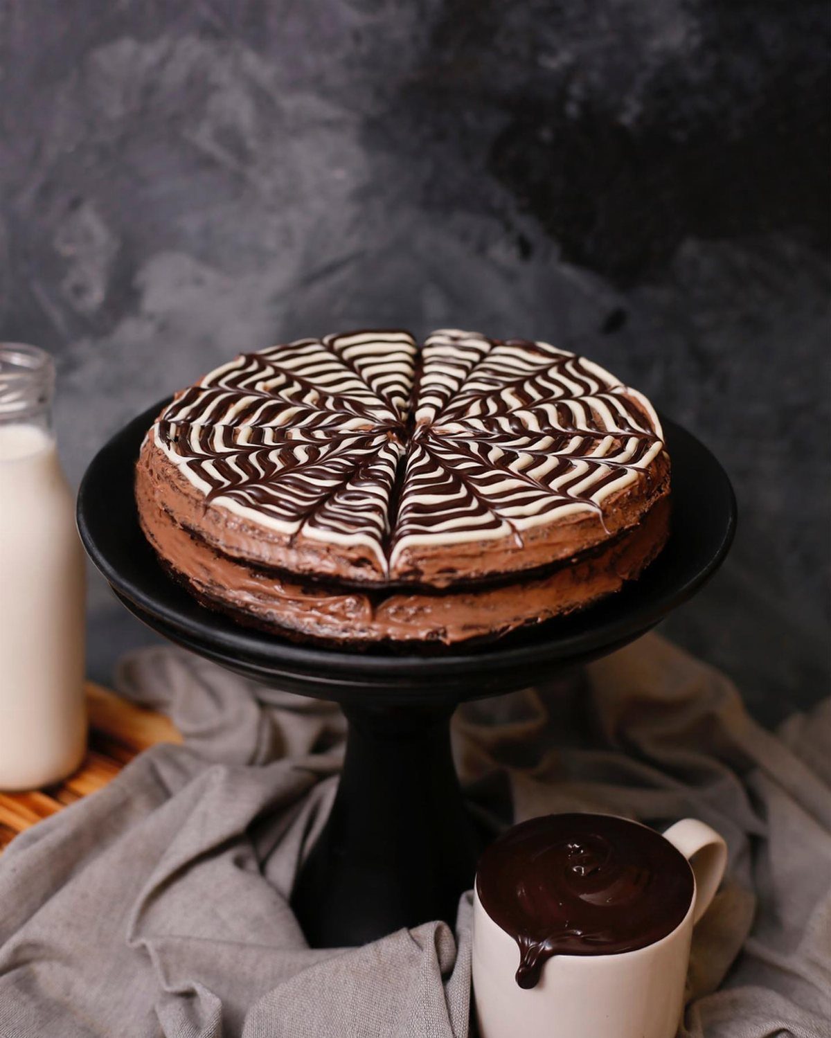 A two-layer chocolate cake with white swirl patterns on a black cake stand.