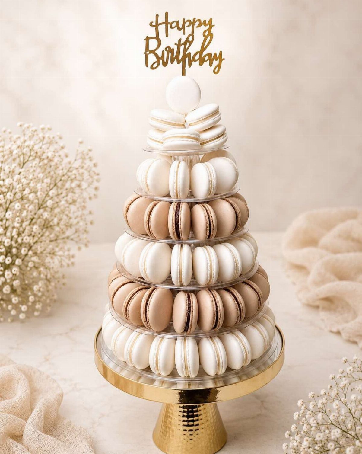 A tiered macaron tower in cream and brown tones with a gold Happy Birthday topper.