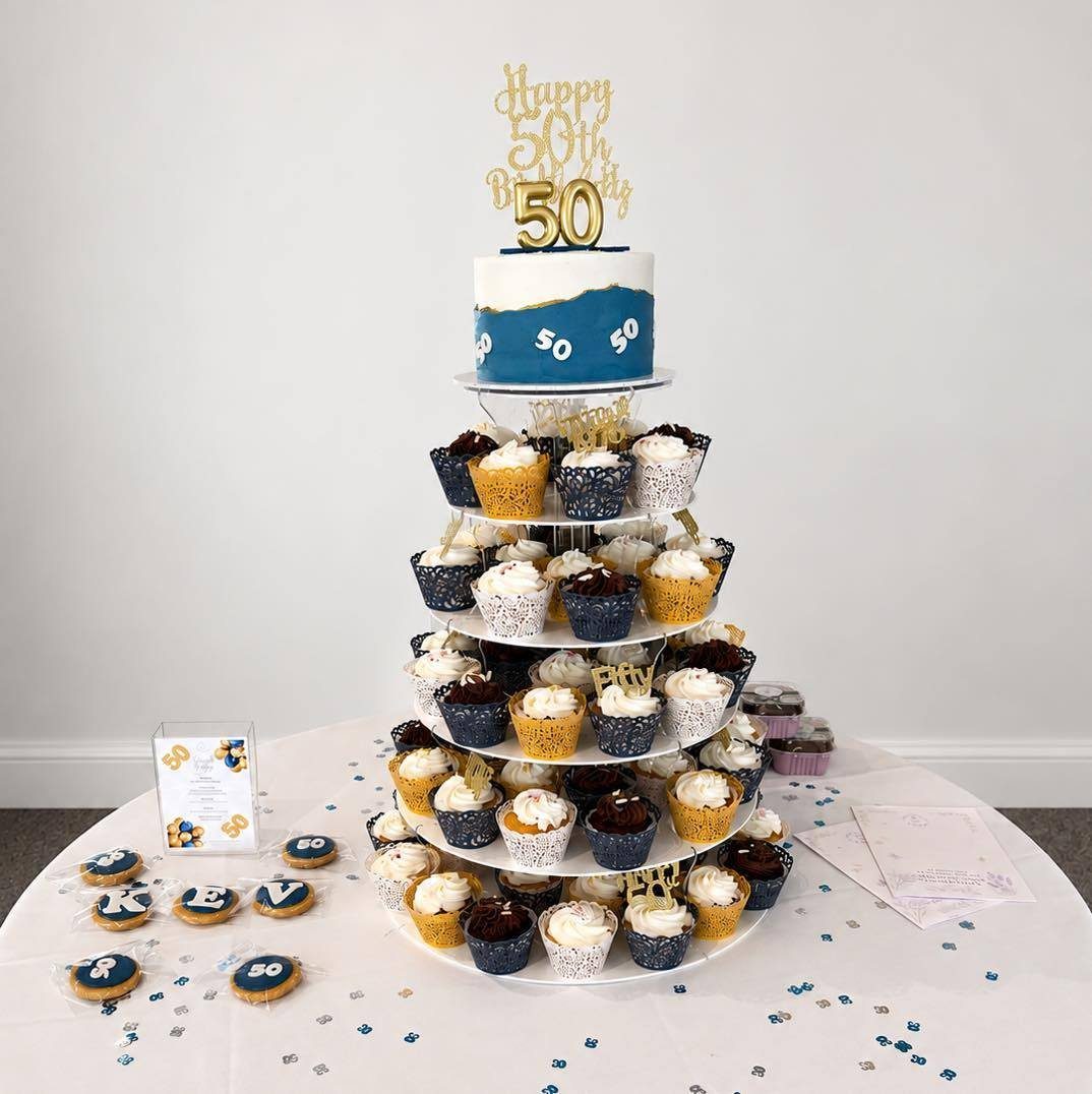 A tiered cupcake tower topped with a blue and gold 50th birthday cake.